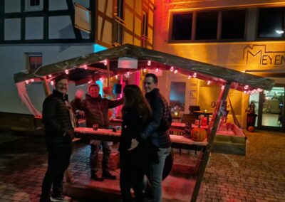 Gäste mit Glühwein an der Hexenhütte mit Kürbis und Lichterketten vor dem Fachwerkhaus des Meyenhof